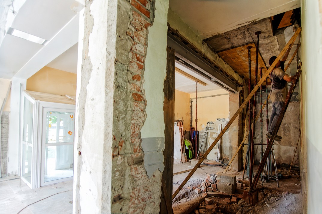 Facharbeiter bei Entkernungsarbeiten im Gebäudeinneren mit abgestützter Decke, freigelegtem Mauerwerk und Stahlträgern während einer Gebäudesanierung.