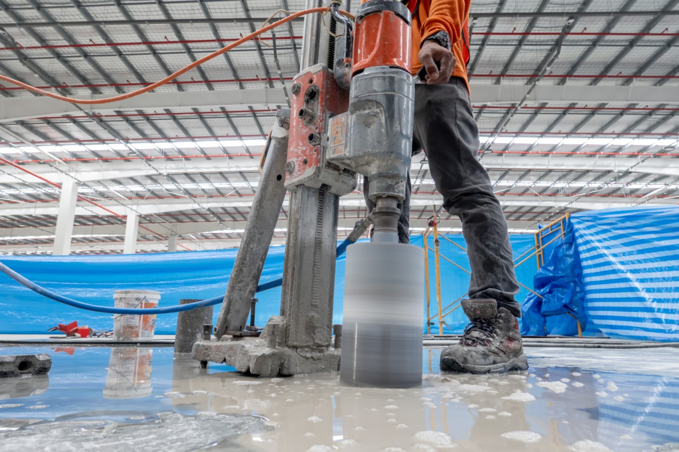 Mitarbeiter führt eine Kernbohrung in einem Betonboden einer Industriehalle mit einer professionellen Diamantbohrmaschine durch.